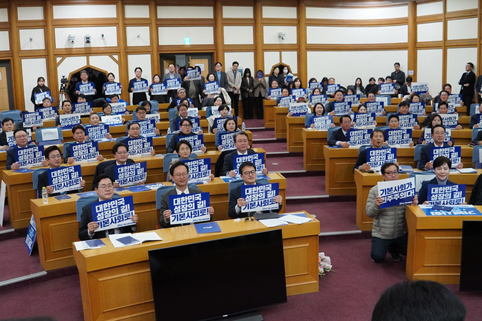 지난 3월11일 서울 여의도 국회 의원회관에서 열린 더불어민주당 서울 기본사회위원회 발대식에서 참석자들이 피켓을 들고 구호를 외치고 있다. 〈민주당 박주민 의원실 제공〉