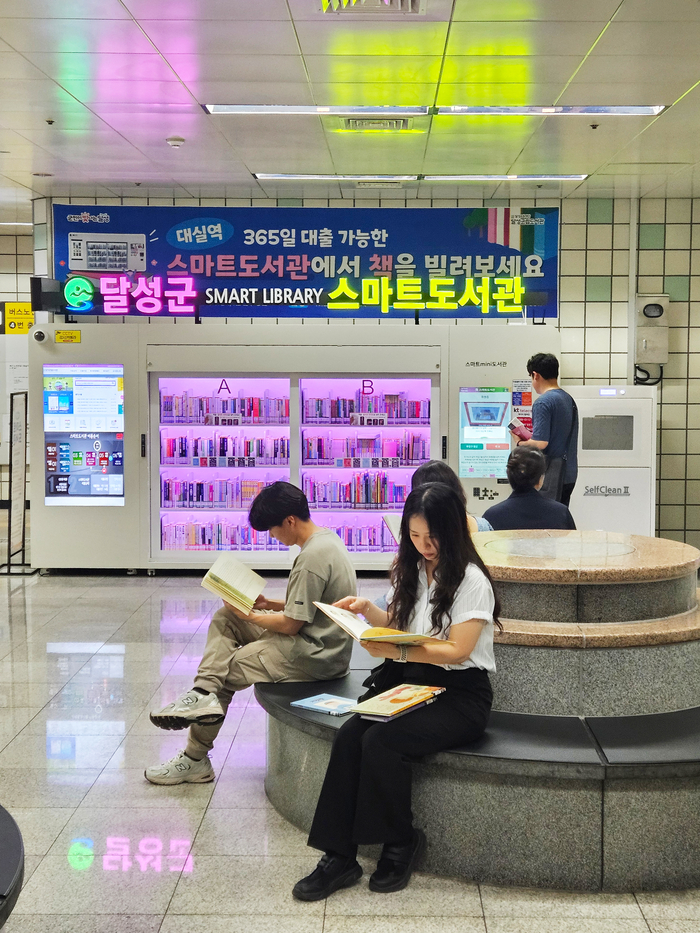 대구도시철도 2호선 대실역 지하 1층 중앙로비에 정식 운영을 시작한 '스마트도서관' 앞에서 시민들이 책을 대출해 읽고 있다.<달성군 제공>
