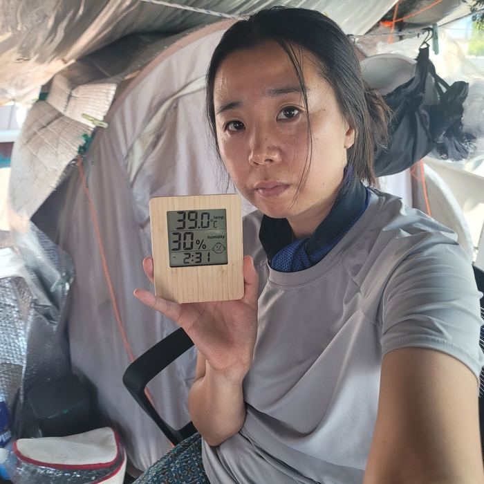 박정혜 금속노조 한국옵티칼하이테크지회 부지회장이 올해 여름 옥상에서 고공농성 중 온도계를 들어보이고 있다. 텐트 안 온도는 39℃이지만 옥상 바닥 온도는 50℃가 넘는다. <박정혜씨 제공>
