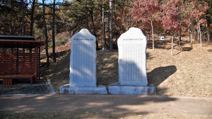 데크 길이 널찍한 임도로 바뀌는 물가에 광장이 있고, 영주댐 수몰지 이주민 512명의 이름에 새겨진 비석이 호수를 바라보며 서 있다.