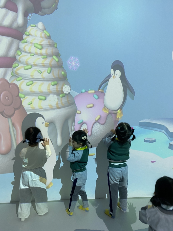 가상현실 미디어 체험공간에서 아이들이 움직이는 캐릭터를 따라 손을 뻗으며 화면을 터치하고 있다.
