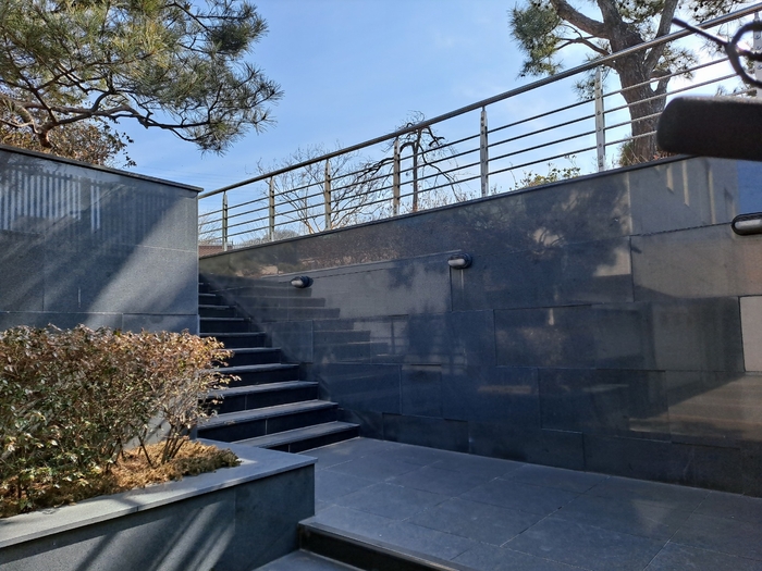 박근혜 전 대통령 달성 사저 입구로 이어지는 계단. 짙은 회색 석재로 마감된 벽면과 계단이 단정한 분위기를 이루며, 금속 난간과 낮은 조경수가 어우러져 있다. 강승규 기자