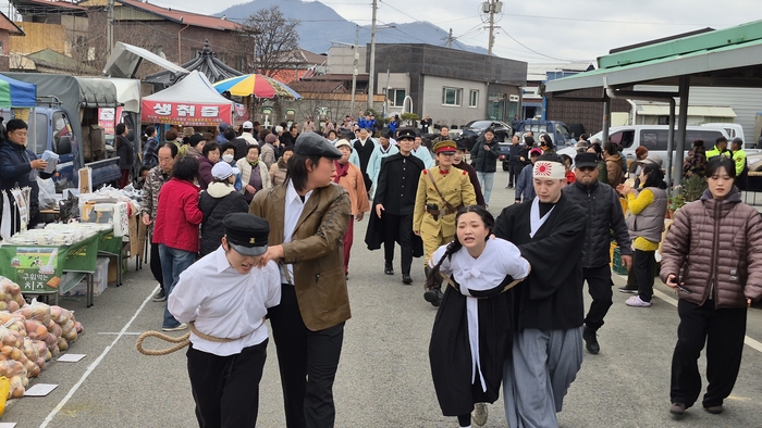 일본 형사에 포박당한 시위학생을 필두로 거리퍼레이드단이 장터에 들어서고 있다.