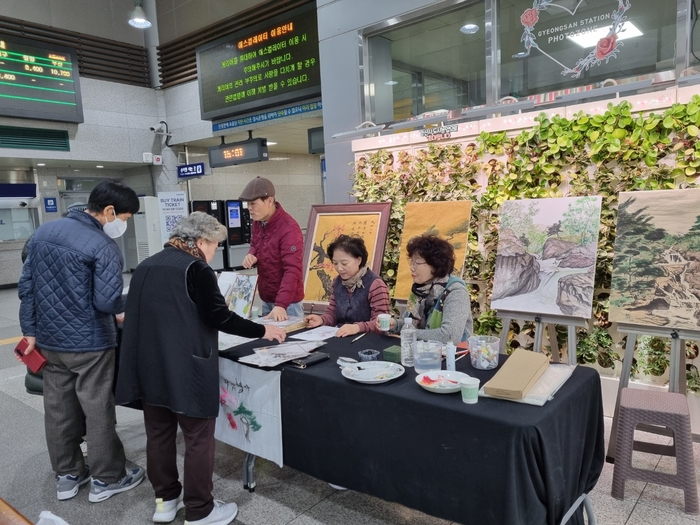 지난달 27일 글·그림동아리 회원들이 경산역 맞이방에서 시민들에게 그림을 그려 나눠주고 있다. 천윤자 시민기자