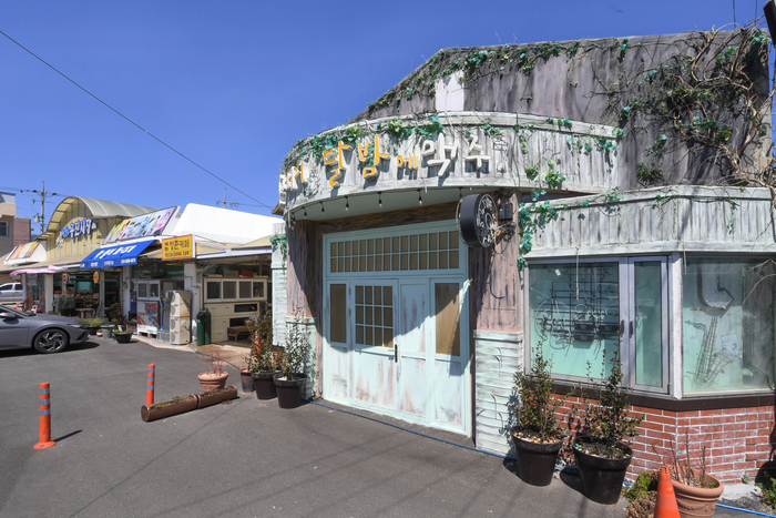 드라마 갯마을차차차의 주요 로케이션이었던 한낮에 커피 달밤에 맥주. 이곳의 커다란 파스텔 톤의 문은 인기 많은 포토존이다. 카페 안쪽 공간은 쉼터로 꾸며져 있다.