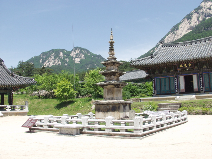 문경 봉암사 경내에 자리한 삼층석탑 전경. 낮은 석재 난간으로 둘러싸인 탑이 중앙에 서 있고, 뒤로는 단청이 화려한 전각과 기와지붕 건물이 이어진다.<강남진기자>