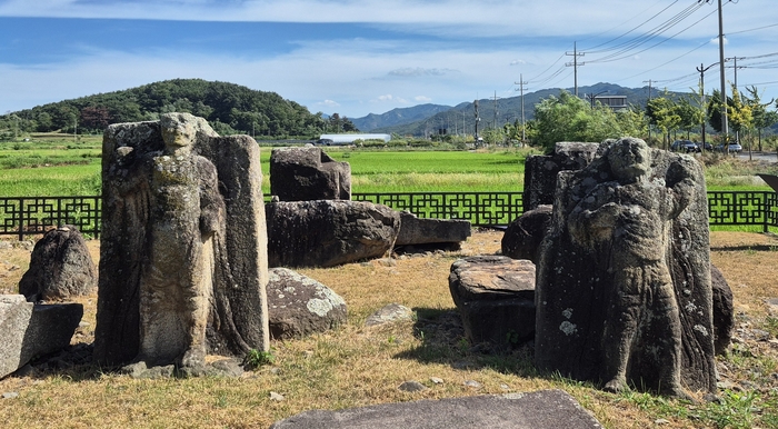 경주시 구황동 모전석탑지에 남아 있는 금강역사상 2구. 서로 다른 자세로 서 있는 두 금강역사의 뒤로 옛 탑의 석재와 한여름 들녘이 펼쳐져 있다. <장성재 기자>