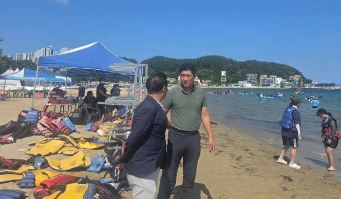이경환 포항시체육회 해양스포츠팀장(오른쪽)이 강원도 사무국장과 함께 지난 5일 영일대해수욕장에서 열린 2026 사회배려계층 해양레포츠 체험교실 현장을 둘러보며 이야기를 나누고 있다. 뒤편 백사장에는 참가자들이 착용할 구명조끼가 가지런히 놓여 있고, 바다에서는 아이들이 카약과 패들보드를 타며 체험을 즐기고 있다. 김기태기자